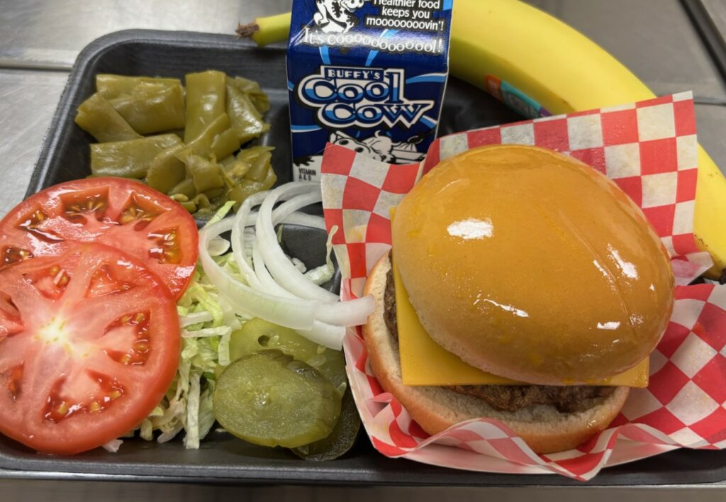 School lunch tray with cheeseburger, toppings, green beans, banana, and a milk.