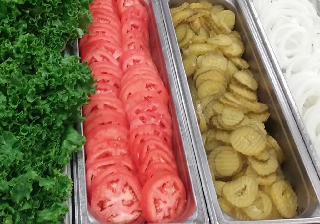 Sliced onions, pickles, tomatoes, and lettuce for toppings.