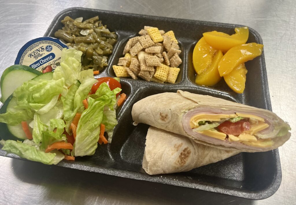 Honey Mustard Turkey Wrap, peaches, cereal mix snack, beans, and salad on a tray.