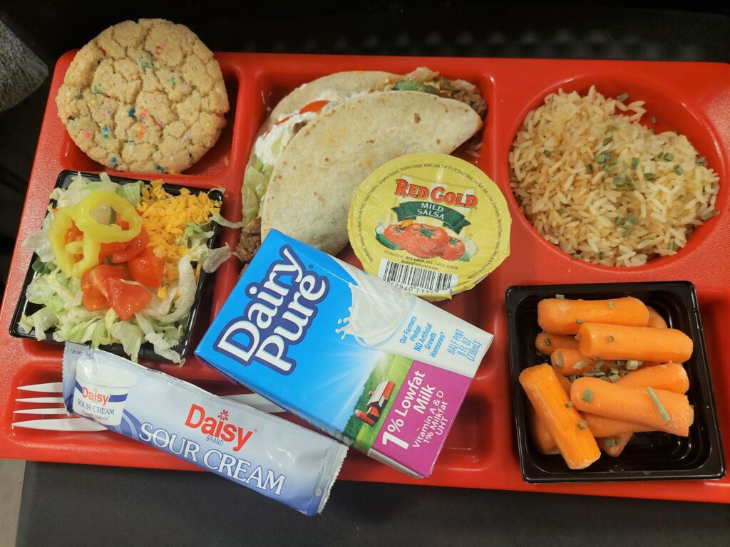 School lunch tray with a taco, rice, salad, honey roasted carrots and a cookie.