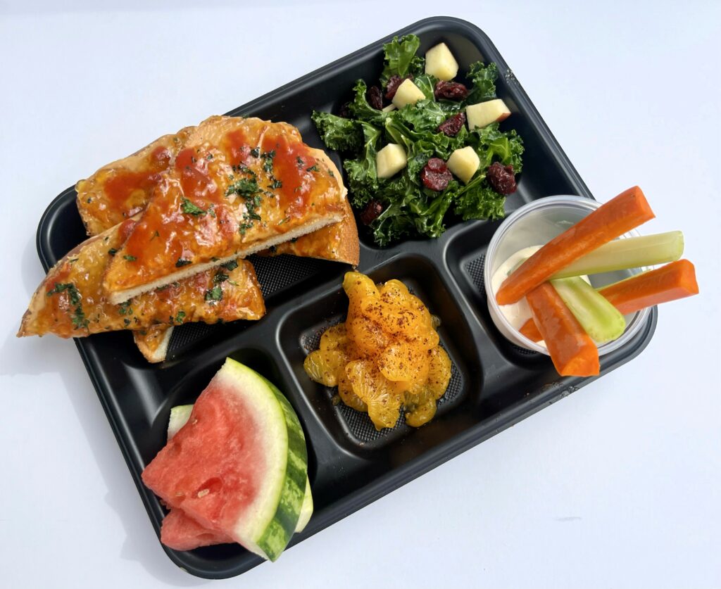 School lunch tray with Sweet and Spicy PBJ, kale salad, fresh fruit and veggie dippers in ranch dressing.