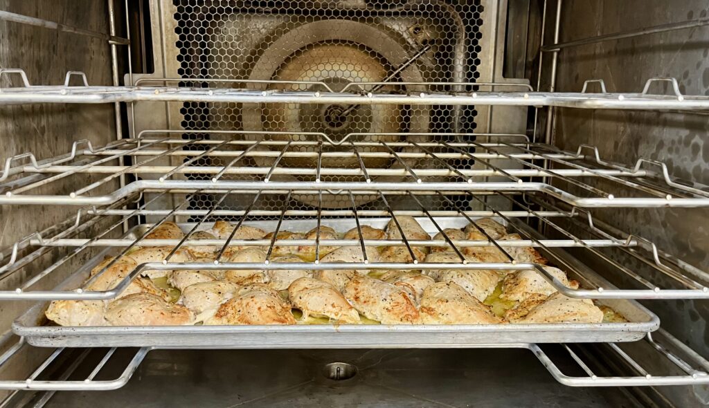 Seasoned chicken in oven on baking sheet.