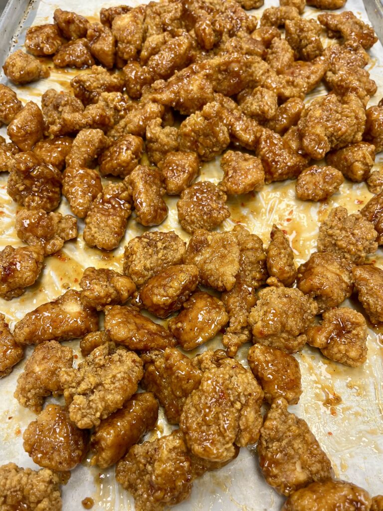 Chicken tossed in orange glaze on pan.