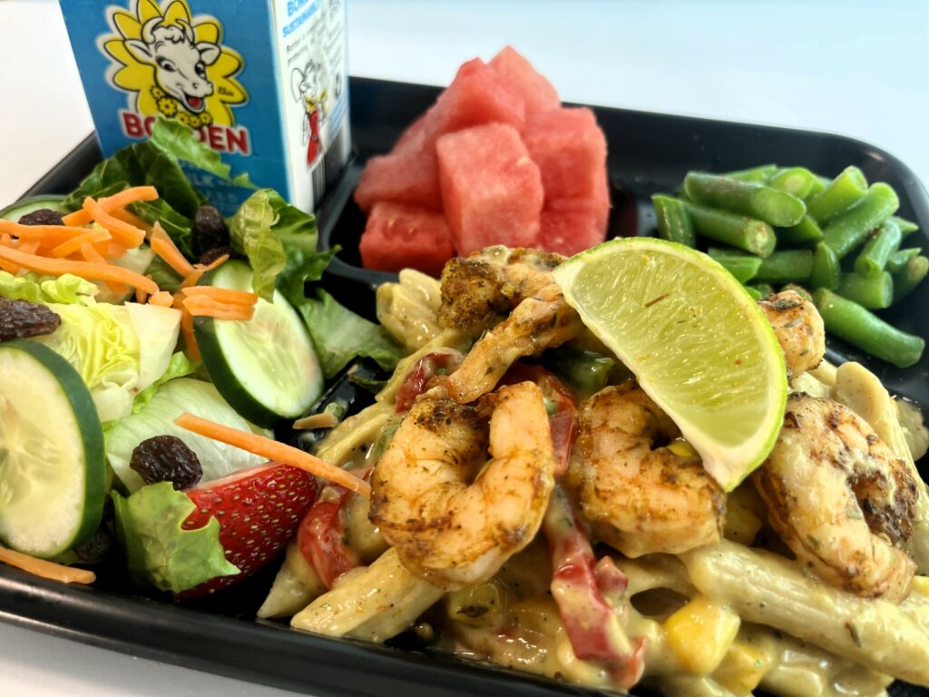 Jamaican Jerk Shrimp Pasta on school lunch tray with watermelon, green beans, salad, and milk.