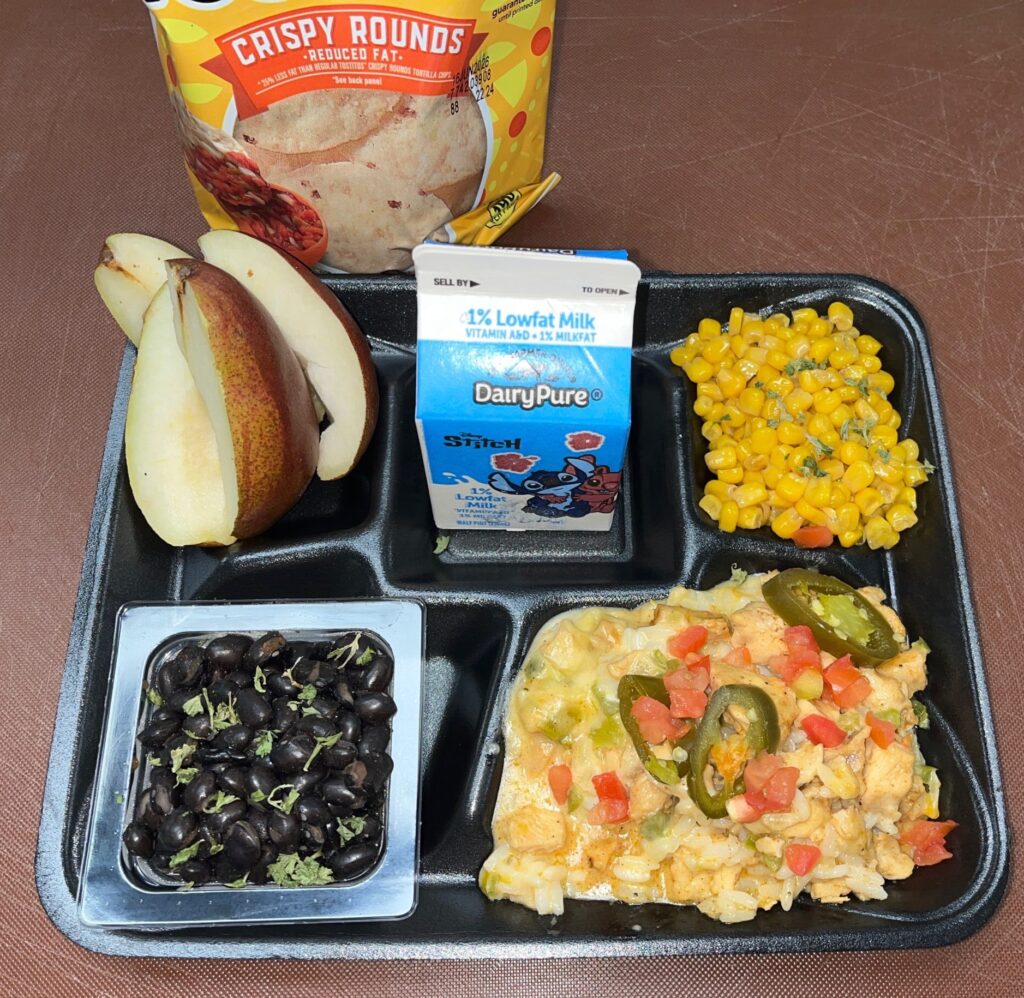 School lunch tray with nachos, fresh pairs, seasoned corn and black beans served with milk.