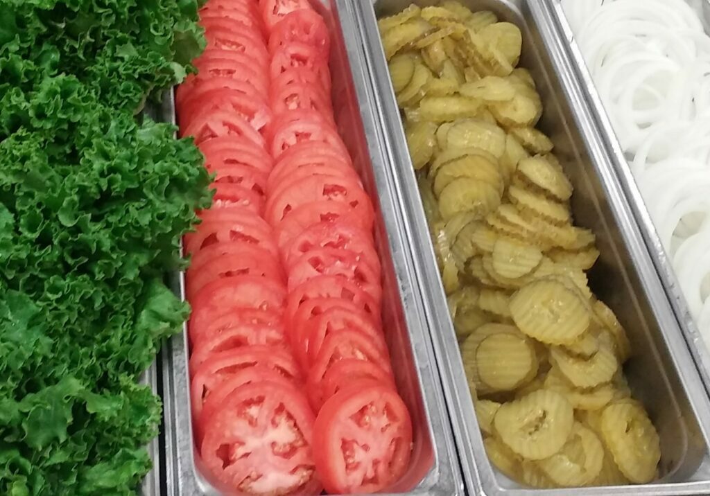 Sliced onions, pickles, tomatoes, and lettuce for toppings.