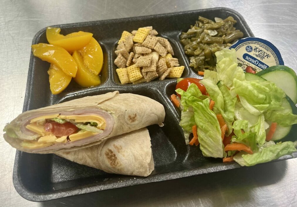 Honey Mustard Turkey Wrap, peaches, cereal mix snack, beans, and salad on a tray.