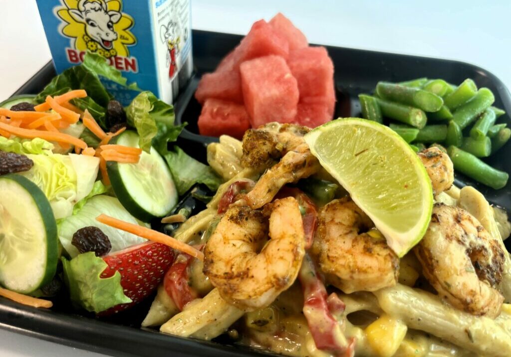 Jamaican Jerk Shrimp Pasta on school lunch tray with watermelon, green beans, salad, and milk.