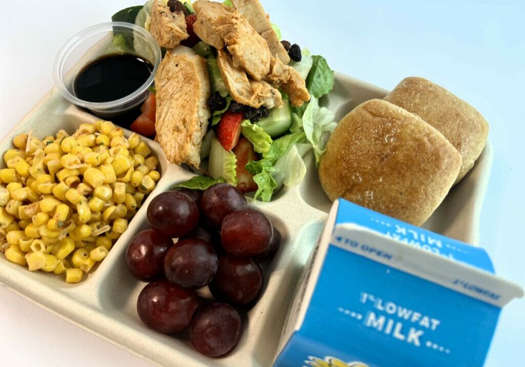 School lunch tray with Harvest Salad with Strawberries, chicken and balsamic dressing, rolls, corn, grapes and milk.