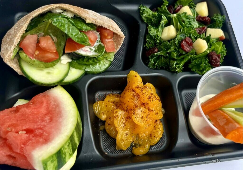 School lunch with White Bean & Veggie Pita, kale salad, watermelon, oranges, and veggie dippers.