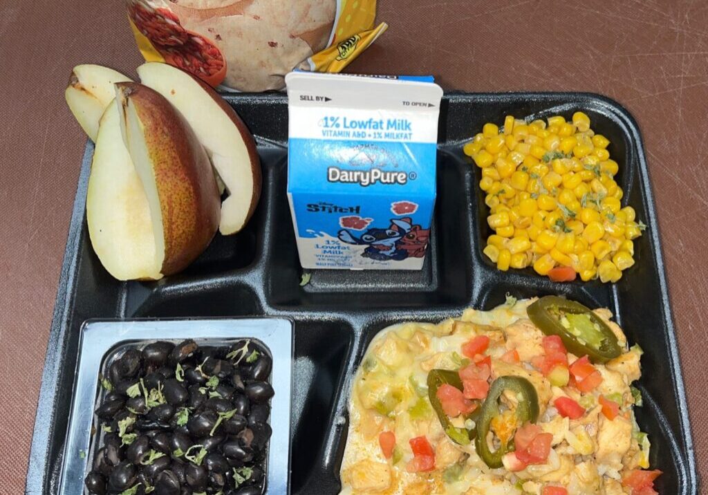 School lunch tray with nachos, fresh pairs, seasoned corn and black beans served with milk.